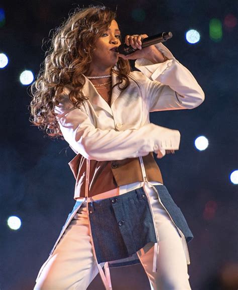 A Woman With Long Hair And White Pants On Stage Holding A Microphone In Her Hand