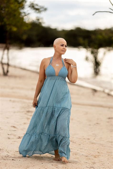 A Bald Woman In A Blue Dress Walking On The Beach With Her Hair Shaved Back