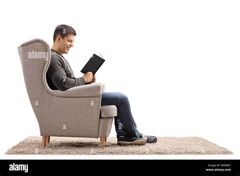 Young Man Seated In An Armchair Reading A Book Isolated On White