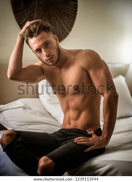 Shirtless Sexy Male Model Lying Alone On His Bed In His Bedroom Looking At Camera With A