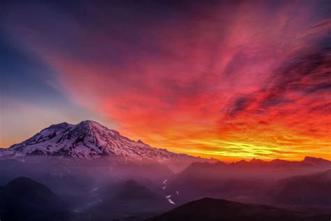 The Sun Is Setting Over A Mountain With Clouds In The Sky And Snow On It