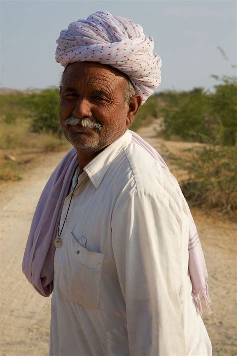 A Man With A Turban On His Head Standing In The Middle Of A Dirt Road