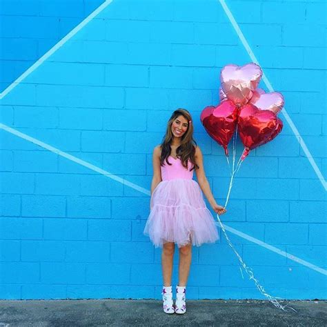 A Girl In A Pink Dress Holding Two Heart Shaped Balloons Against A Blue