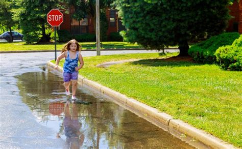 Toddler Girl In Jumping In Puddles After Summer Rain Stock Photo