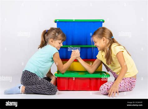Two Girls Fight On Hands Putting Elbows On A Box With Toys Stock Photo