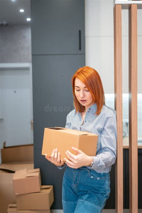 Young Woman Moving Into New Apartment Holding Cardboard Boxes Stock