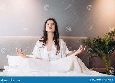 Young Beautiful Woman In White Silk Pajamas Is Doing Yoga In The