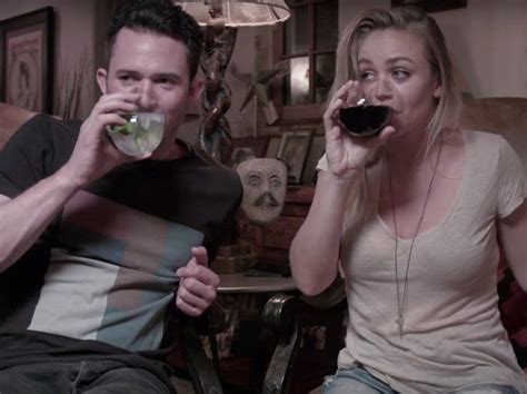 A Man And Woman Sitting On A Couch Drinking From Wine Glasses In Front Of Them