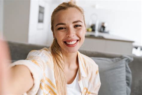 Happy Blonde Woman Smiling While Taking Selfie Photo At Home Stock