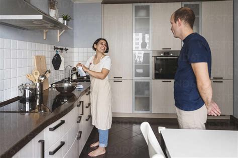 Smiling Wife Talking To Husband While Preparing Food In Kitchen At Home Stock Photo