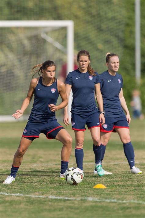 three female soccer players in blue uniforms are on the field playing with a soccer ball