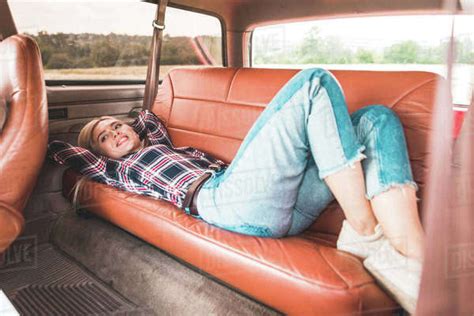 Beautiful Young Woman Lying On Back Seat Of Vintage Car In Field