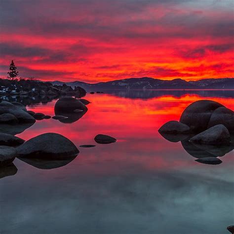 The Sky Is Red And Orange As It Reflects In The Still Water At This Lake