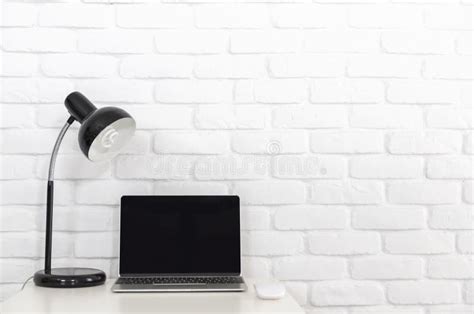 A Blank Screen Laptop Computer On White Desk With Lamp And White Brick