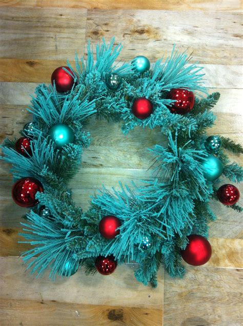 a christmas wreath with red and green ornaments on it sitting on a wooden floor next to a pair