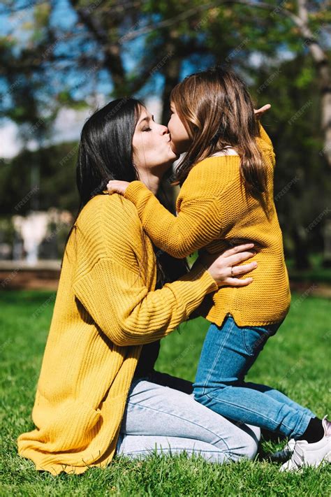 Premium Photo Side View Of Mother Kissing Daughter While Kneeling On Grassy Field In Park