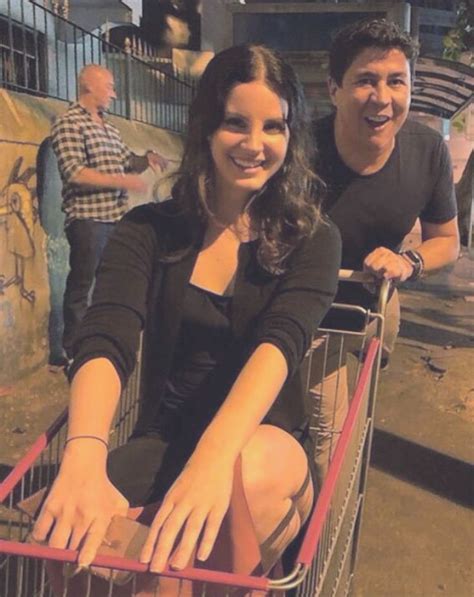 Two People Sitting In A Shopping Cart With One Person Smiling At The Camera And Another Man