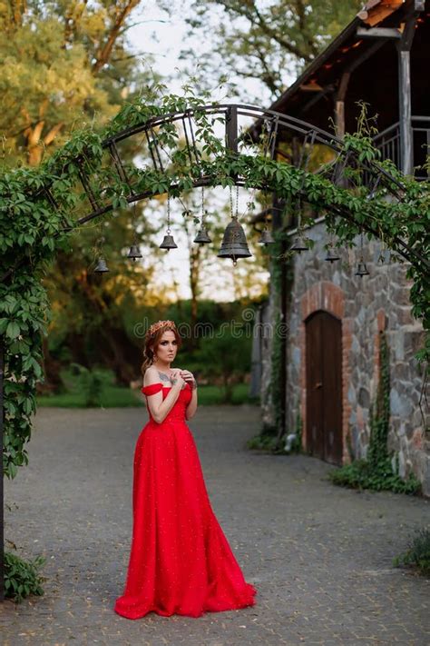 Attractive Redhead Tattooed Woman In Red Dress And Diadema On Blurred