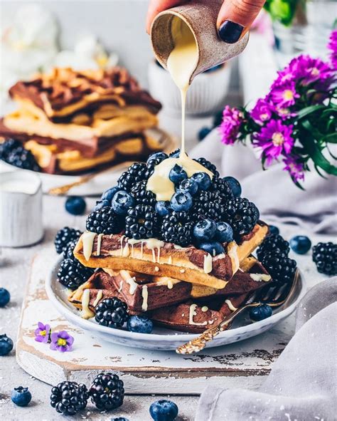 A Person Pouring Syrup On Some Waffles With Blueberries And Other Toppings