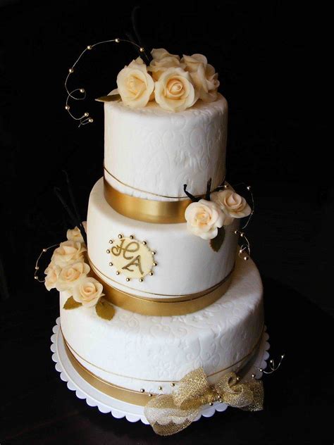 A Three Tiered White Wedding Cake With Gold Trimmings And Flowers On Top