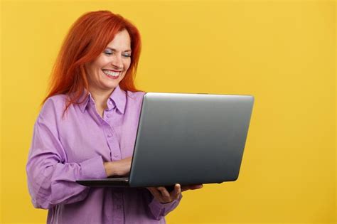 Mujer madura pelirroja sonriendo mientras usa una computadora portátil Foto Premium