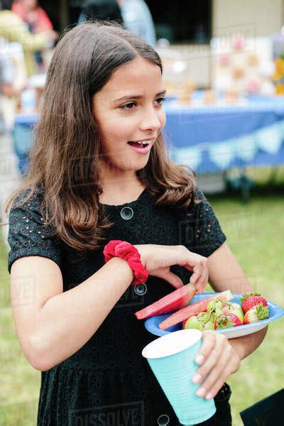 Tween Girl Smiles At A Celebration While Carrying A Plate Of Fruit Stock Photo Dissolve