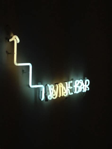 A Neon Sign That Says Wine Bar On The Side Of A Dark Room With Stairs