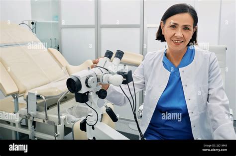 Portrait Of Gynecologist Woman Sitting Near Colposcope And Gynecological Chair In Her Doctors