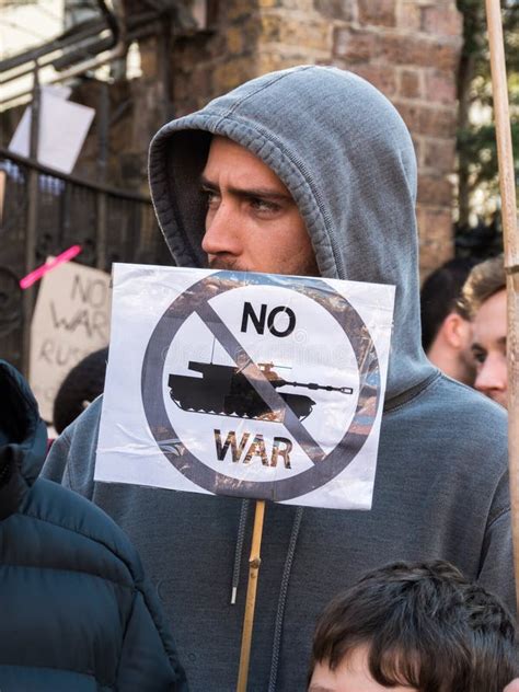 A Protestor Holding A Placard Saying No War Crossed Out Military Tank