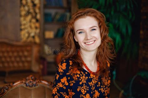 Portrait Of A Beautiful Cheerful Red Haired Young Woman Smiling Looking At The Camera Sitting