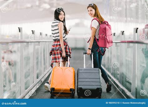 two happy asian girls traveling abroad together carrying suitcase luggage in airport air