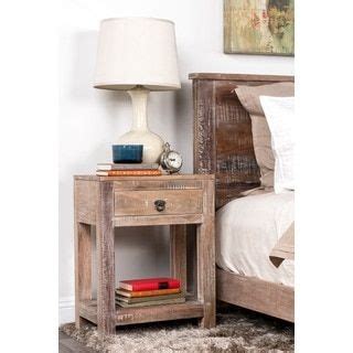A Nightstand With A Lamp On Top Of It Next To A Bed