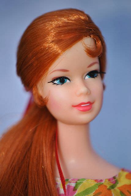 A Doll With Long Red Hair Wearing A Flowered Dress And Pink Necklace On