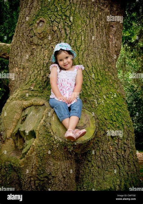 A Little Pre School Girl Sits On The Broken Branch Of A Tree Stock