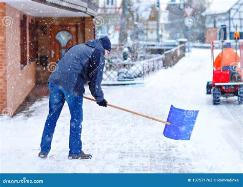 Man With Snow Shovel Cleans Sidewalks In Winter During Snowfall Winter