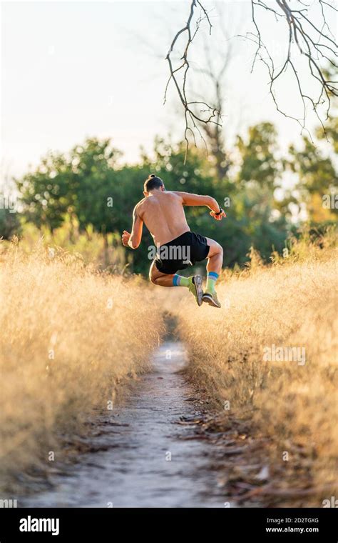 Full Body Back View Of Unrecognizable Shirtless Male Athlete Jumping High Over Narrow Footpath