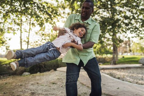 Playful Father Swinging Son While Playing At Park Stock Photo Dissolve