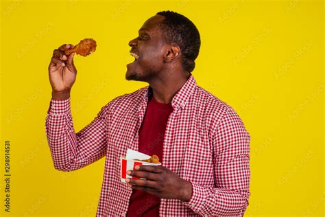 Funny African American Man Eating Fried Chicken Leg In Studio Yellow
