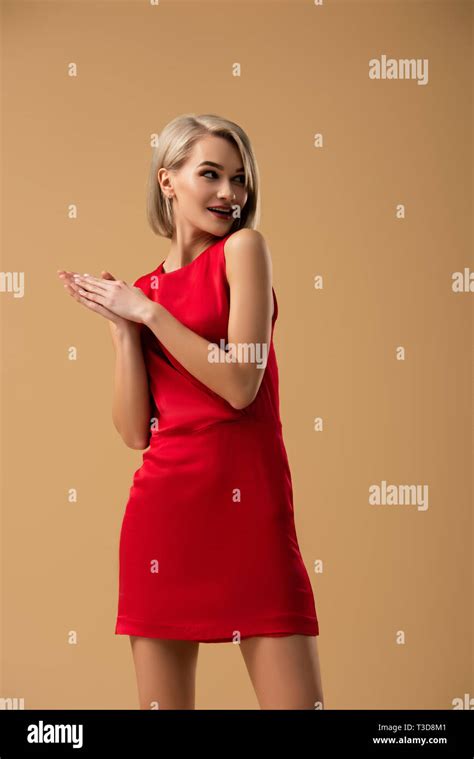 Slim Blonde Girl In Red Dress Looking Away With Smile Isolated On Beige