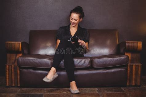 Smiling Woman Sitting On Sofa And Reading A Magazine Stock Image