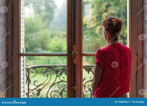 Lady In Red Looking Out A Windows To A Lush Country Garden Outside