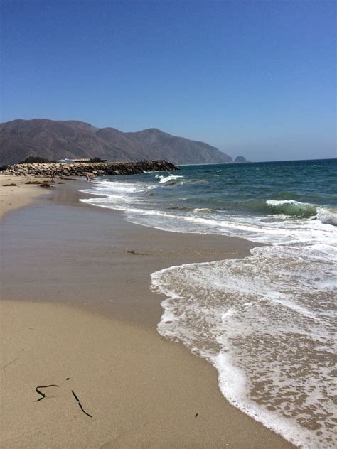 The Beach Has Waves Coming In To Shore And Mountains In The Distance On A Sunny Day