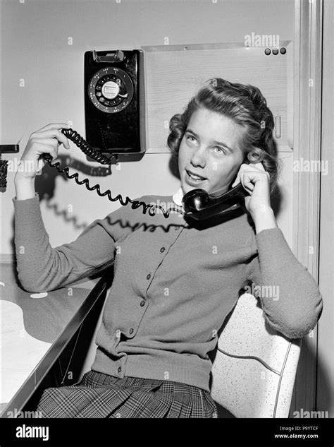 1950s Teenage Girl Talking On Wall Mounted Dial Telephone Holding The
