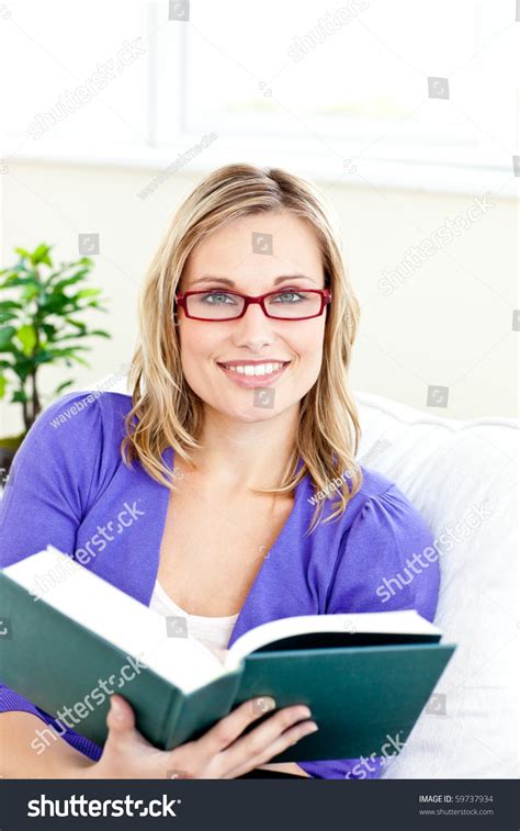 Smiling Young Woman Wearing Red Glasses Reading A Book On A Sofa At