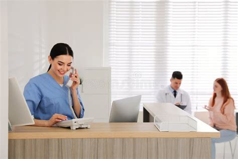Receptionist Talking On Phone While Doctor Working With Patient In