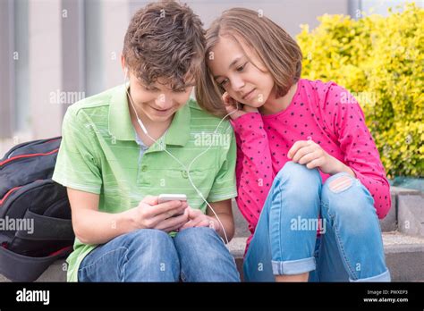 Happy Teenage Boy And Girl With Headphones Are Using Gadget Talking