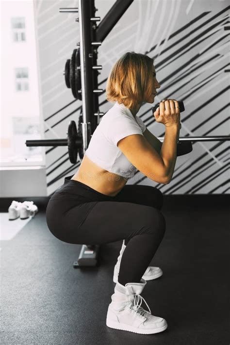 a sporty girl performs squats with dumbbells during a workout in the gym sports fitness body