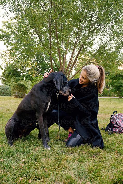 Smiling Woman Stroking Big Black Dog In Park By Stocksy Contributor