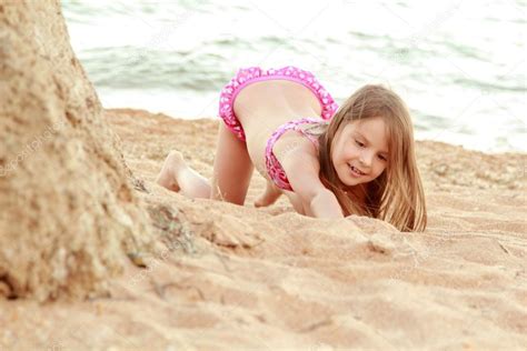 Красивая улыбка маленькая девочка в розовый купальник играет в песке на пляже Стоковое фото