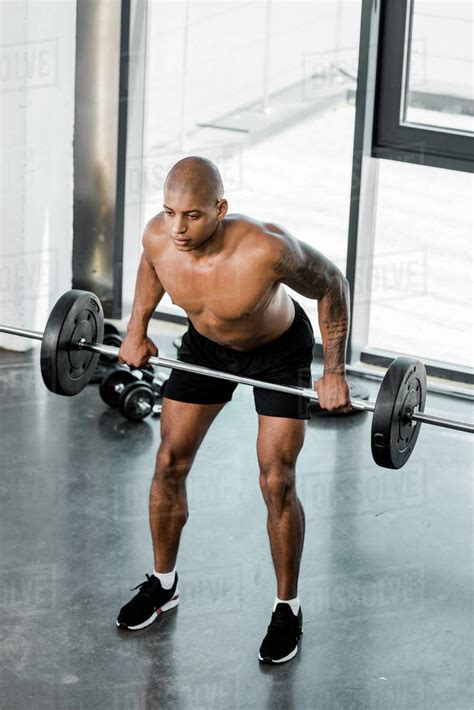 high angle view of muscular bare chested african american sportsman lifting barbell in gym